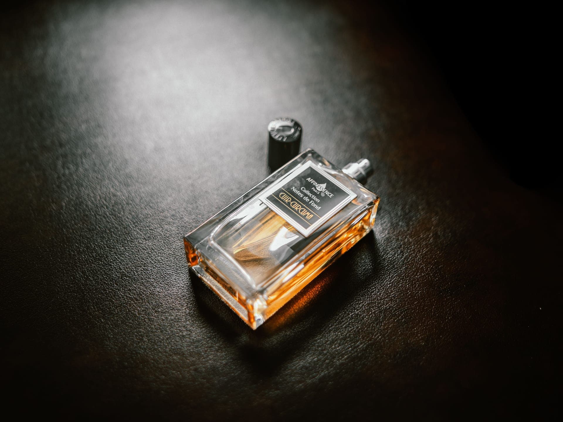 Warm amber fragrance bottles in low, candle-lit shadow